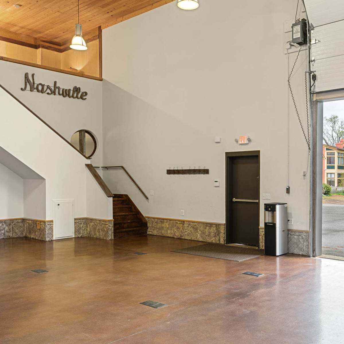 An empty interior space with a staircase on the left, a door leading outside, and a sign that reads "Nashville" on the wall.