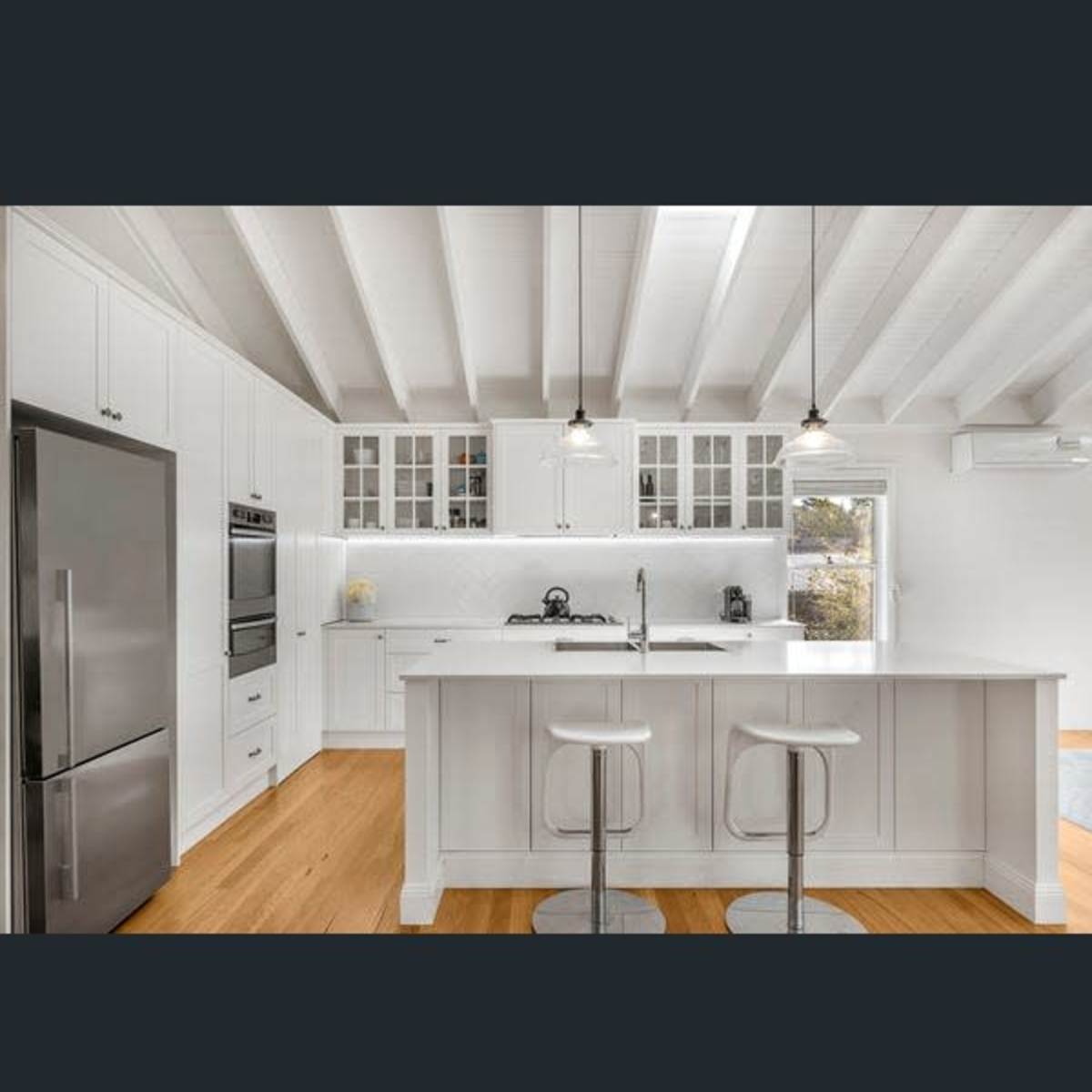 A modern kitchen with white cabinetry, stainless steel appliances, and a central island with two stools.