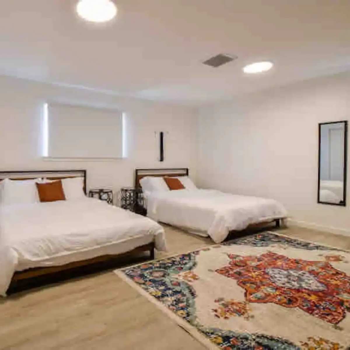 A spacious bedroom with two twin beds, a patterned rug on the floor, and a large mirror on the wall.