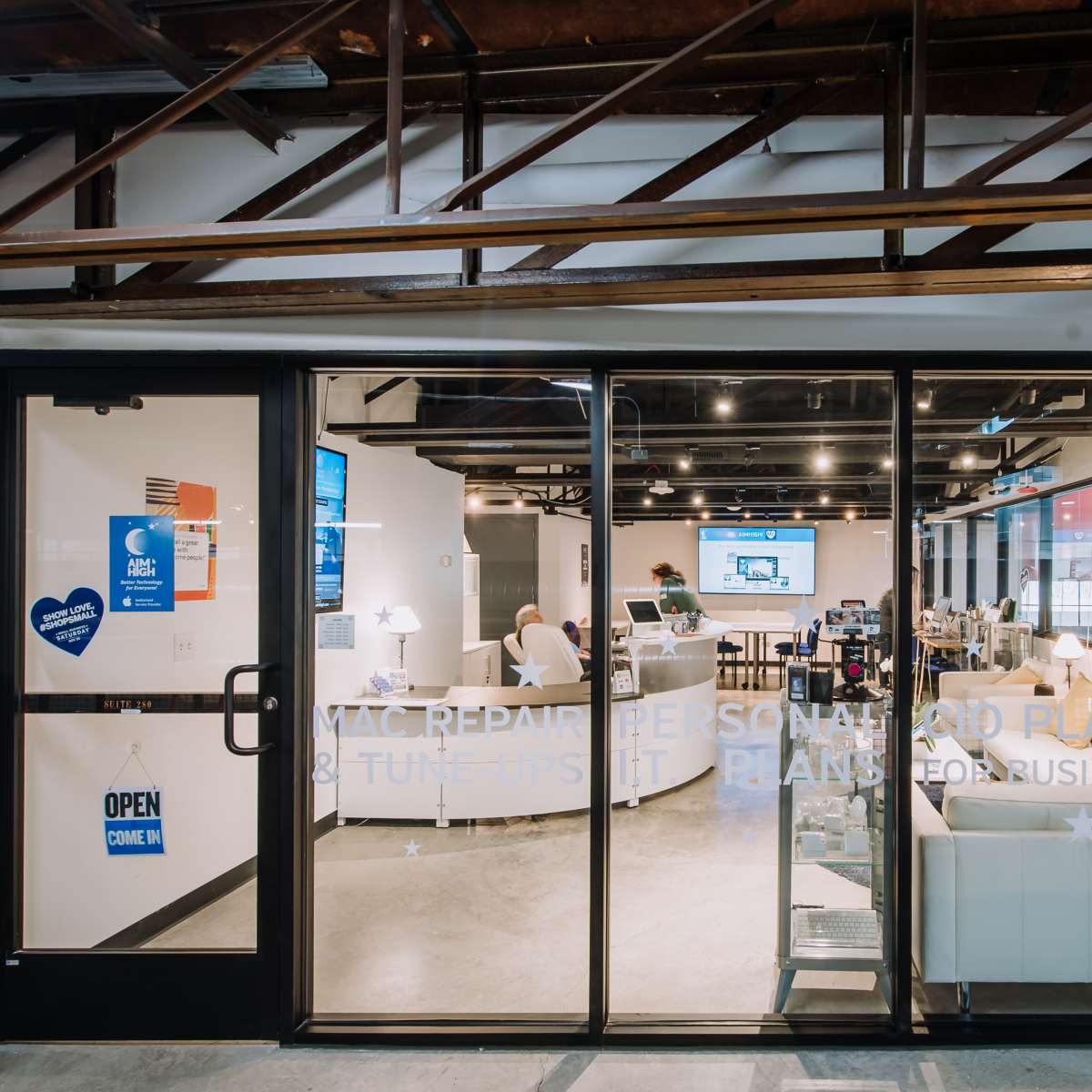 A glass entryway displays a modern office space with seating areas and digital screens visible inside.