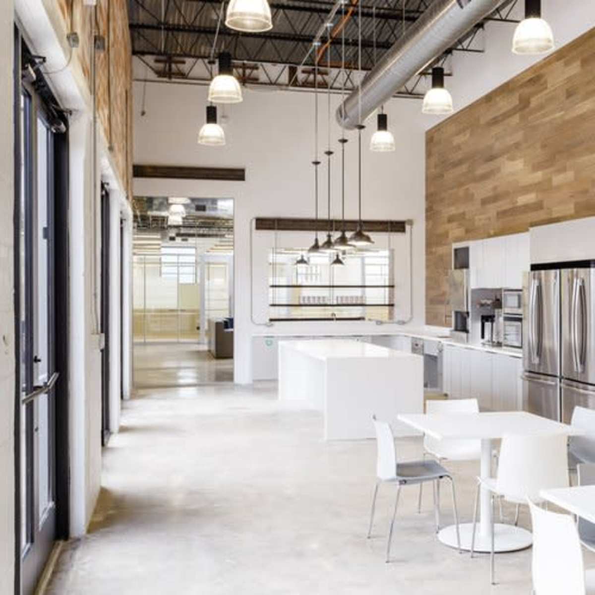A modern kitchen and dining area with white furniture, stainless steel appliances, and a combination of open spaces and wooden accents on the walls.