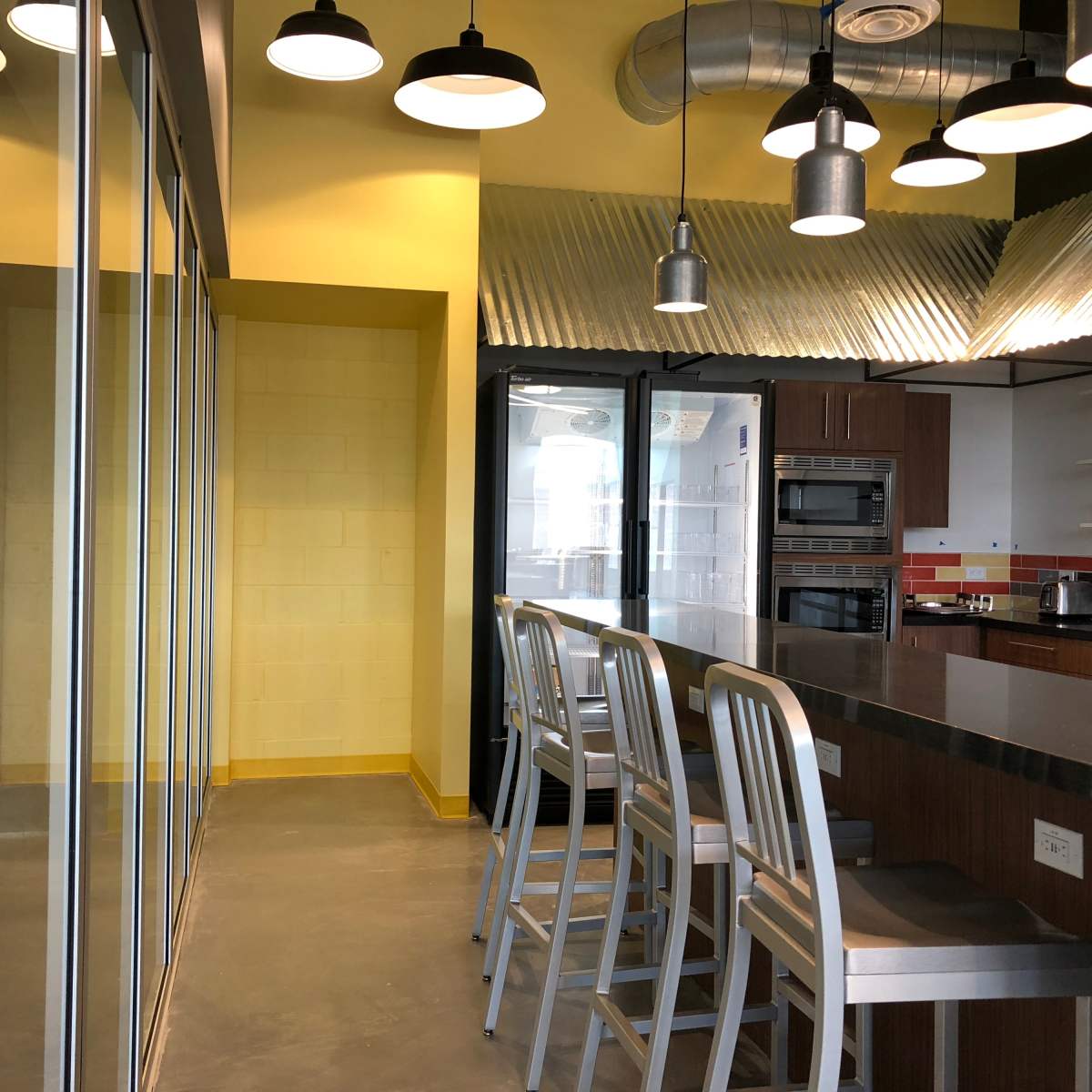 A modern kitchen with metal bar stools, a long counter, and glass-paneled cabinets in a brightly lit space.