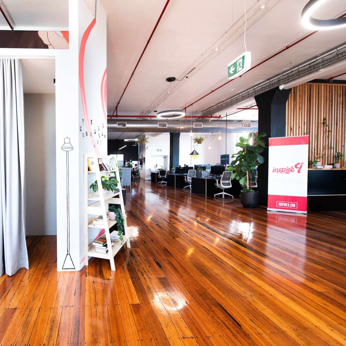 A woman exits a cubicle area in a modern office with wooden floors and contemporary design elements.