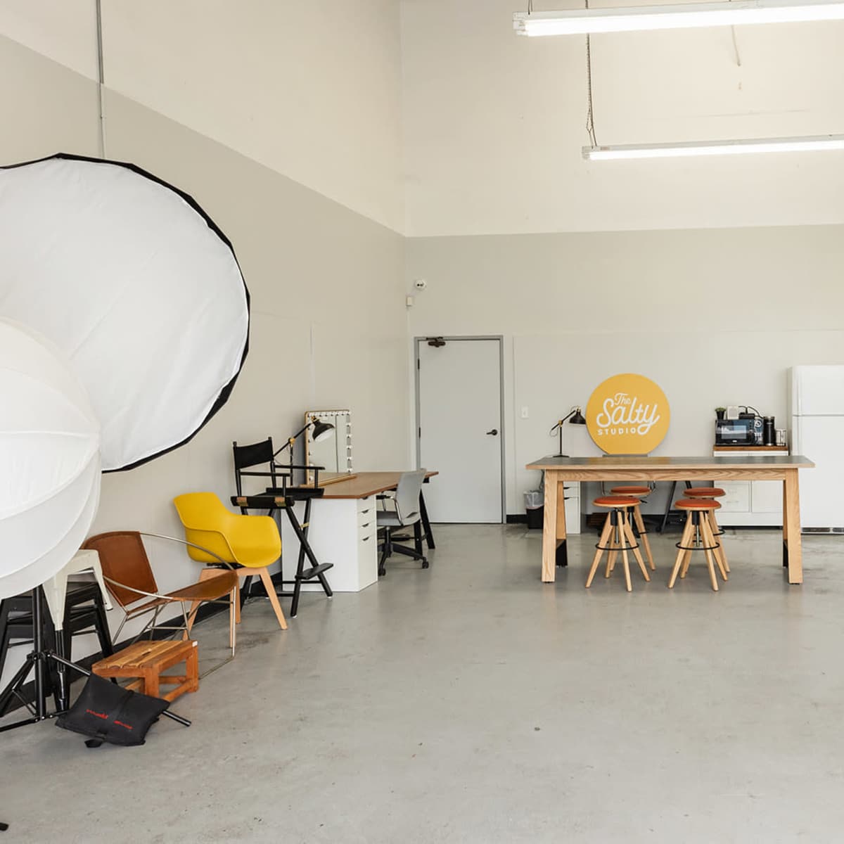 A spacious studio with a table, chairs, and various photography equipment, including large backdrops and lighting setups.