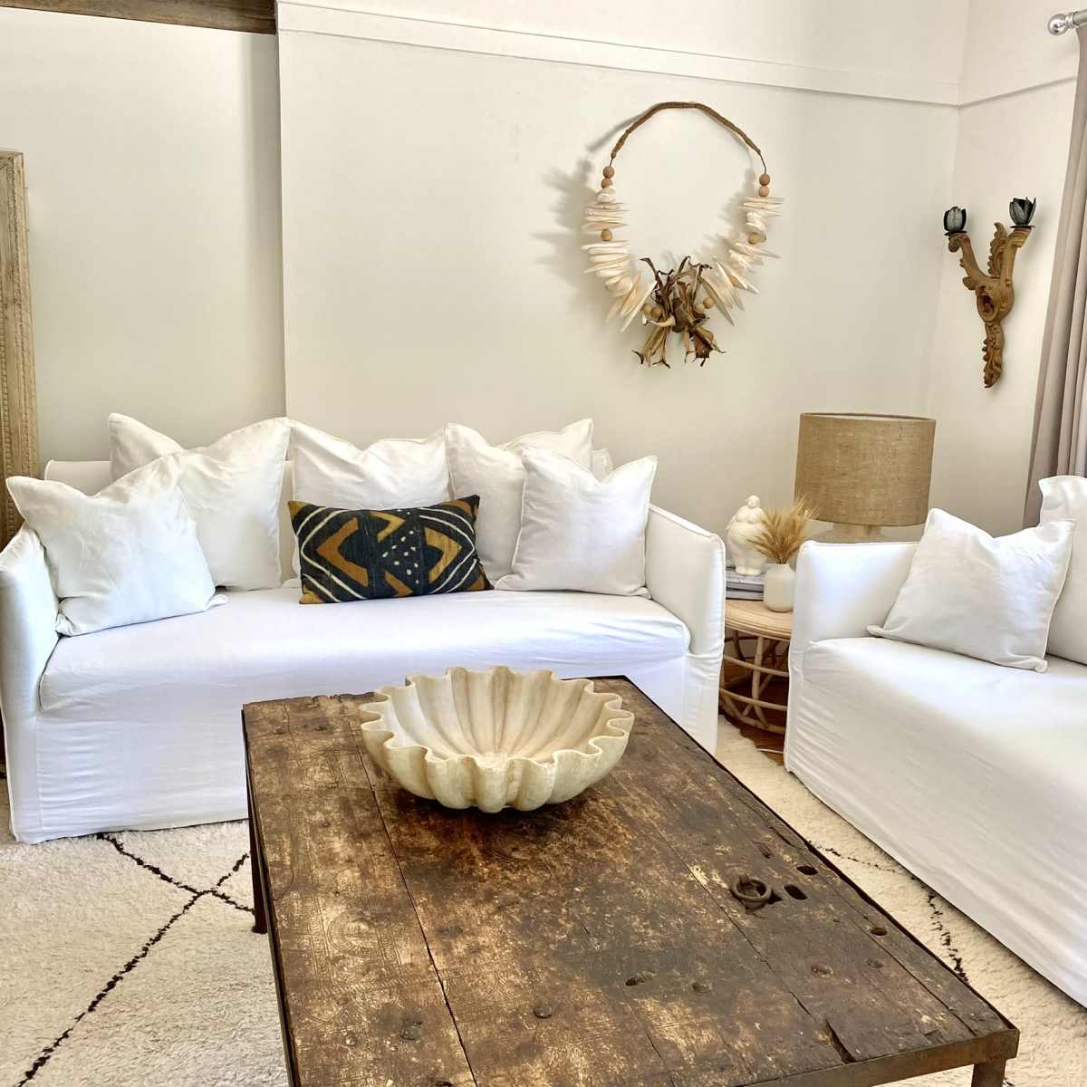 A living room with two white sofas, a wooden coffee table, and decorative elements including a natural fiber bowl and a wall hanging.