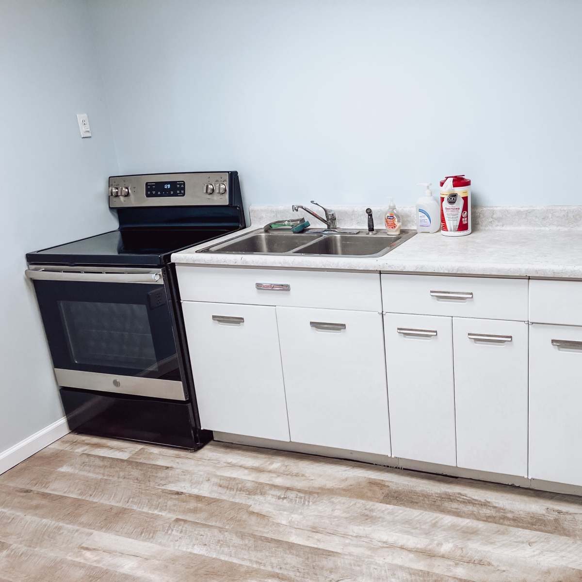 A clean kitchen area with a stainless steel oven, a double sink, and white cabinets situated against a light blue wall.