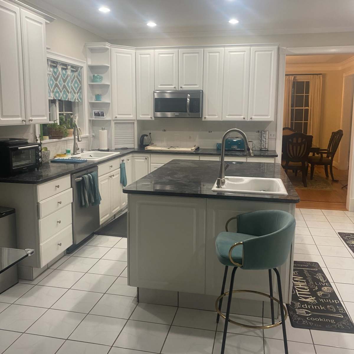 A modern kitchen with white cabinets, a dark countertop, and a central island with a teal bar stool.