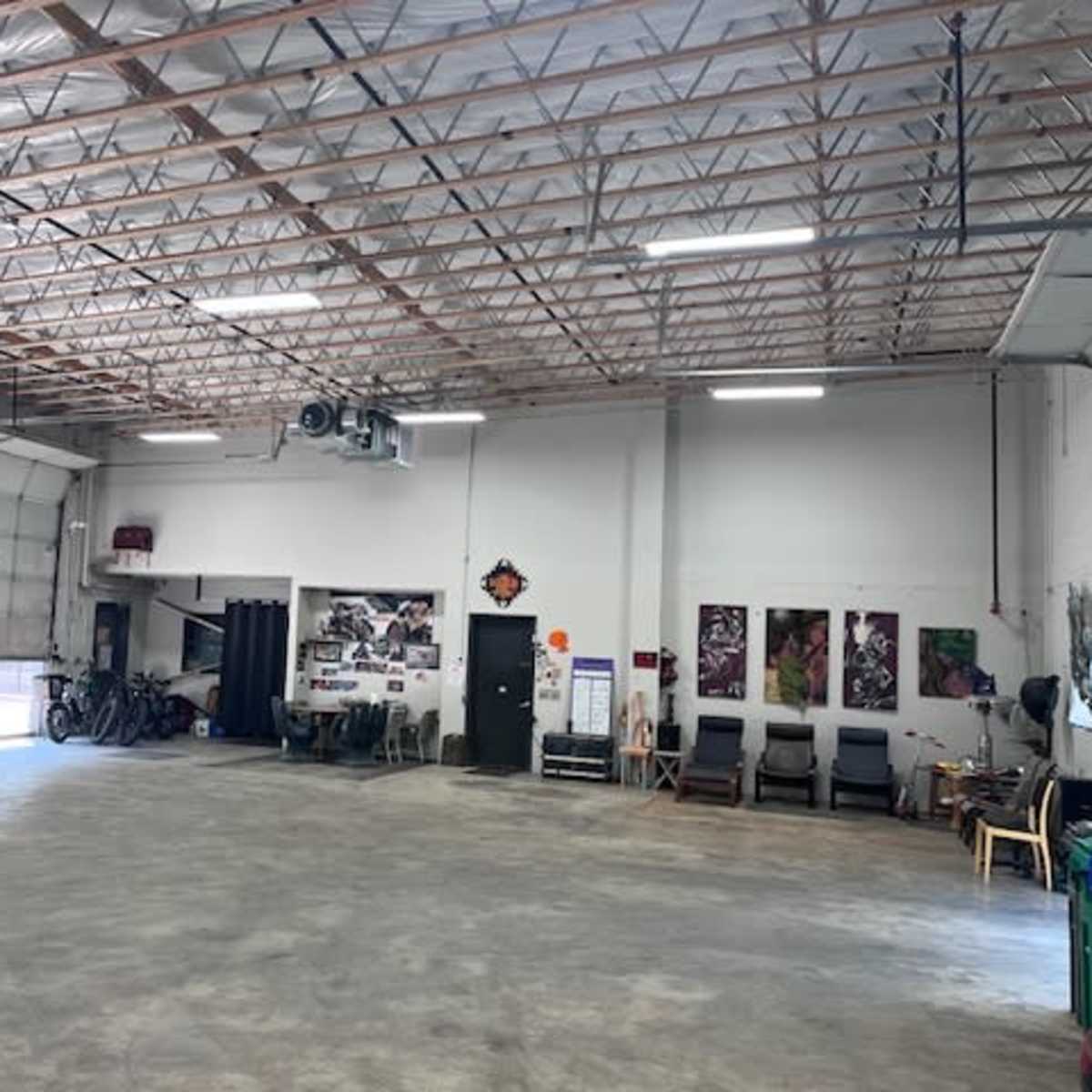 A spacious garage with concrete flooring, open doors, and various items such as bicycles and chairs along the walls.