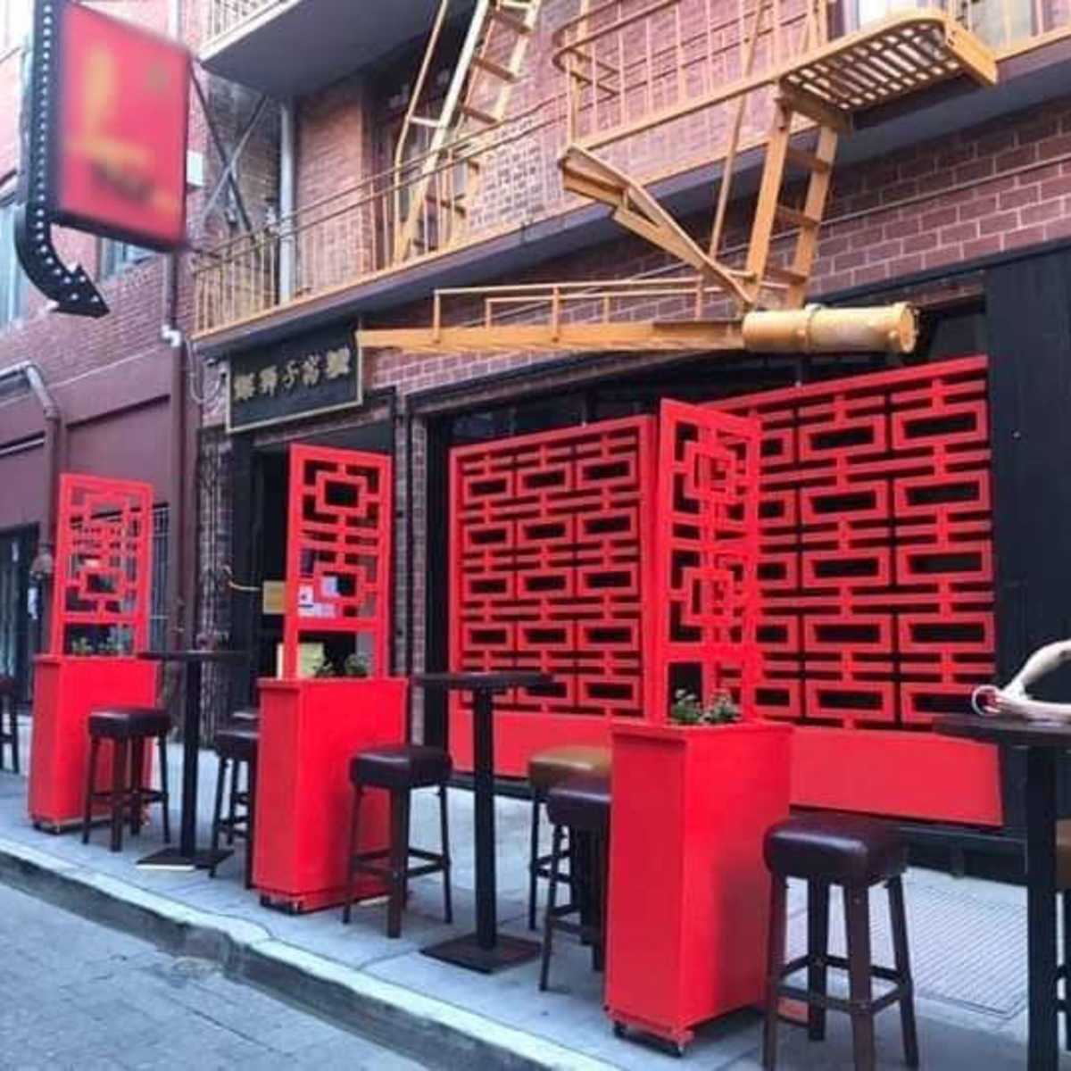 A narrow street with outdoor seating at a restaurant featuring bright red partition screens and tall tables.