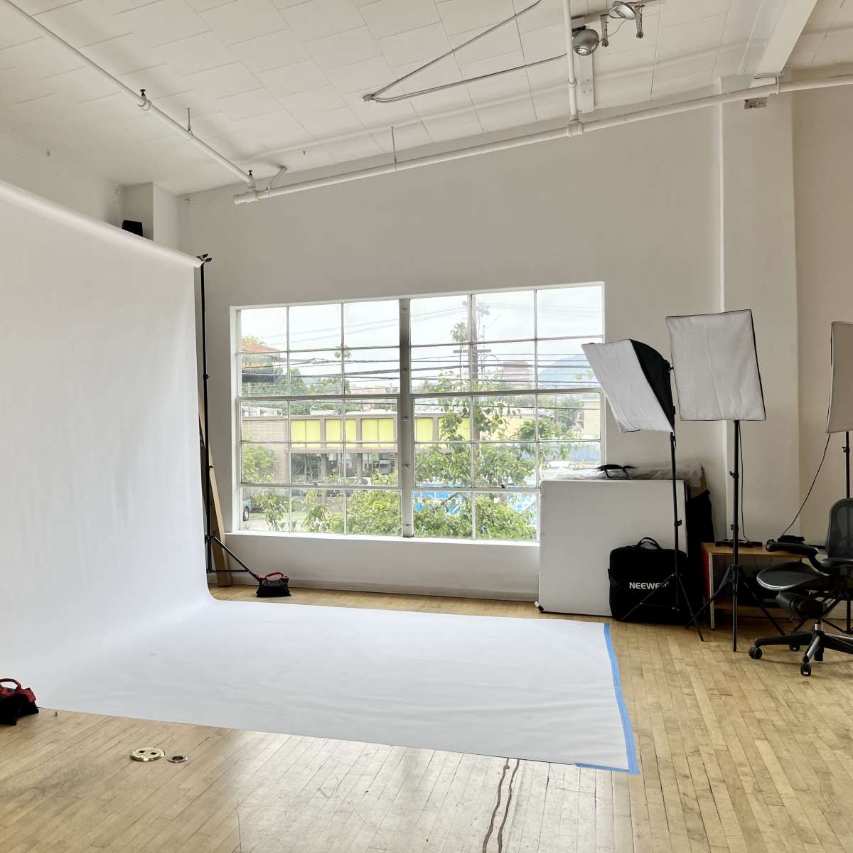 A photography studio with a large white backdrop, two softbox lighting setups, and a window providing natural light.