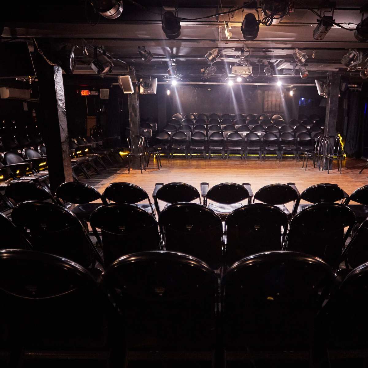 An empty performance venue features a central stage surrounded by rows of black chairs.