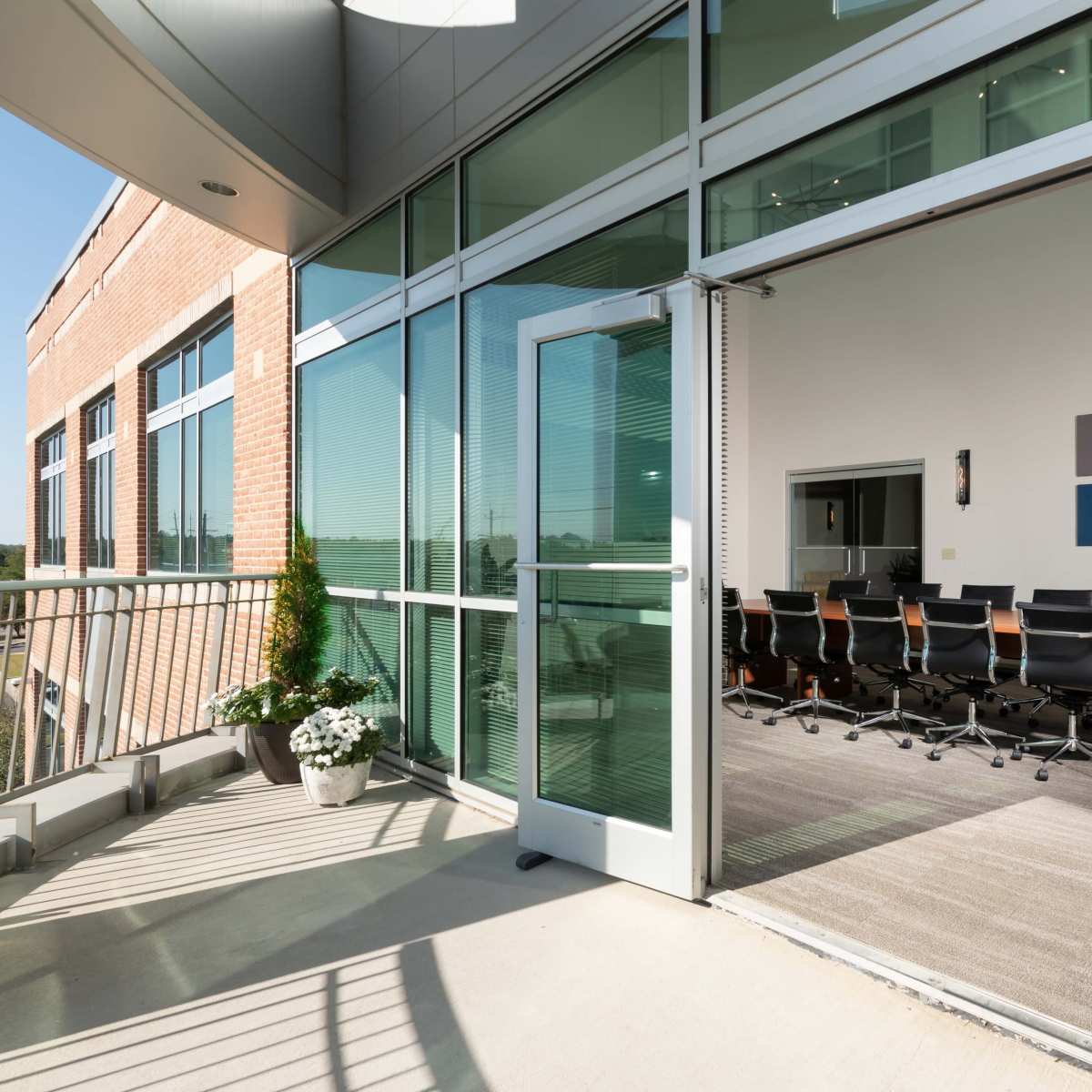A conference room with a long table and multiple chairs is visible through an open sliding glass door on a balcony.