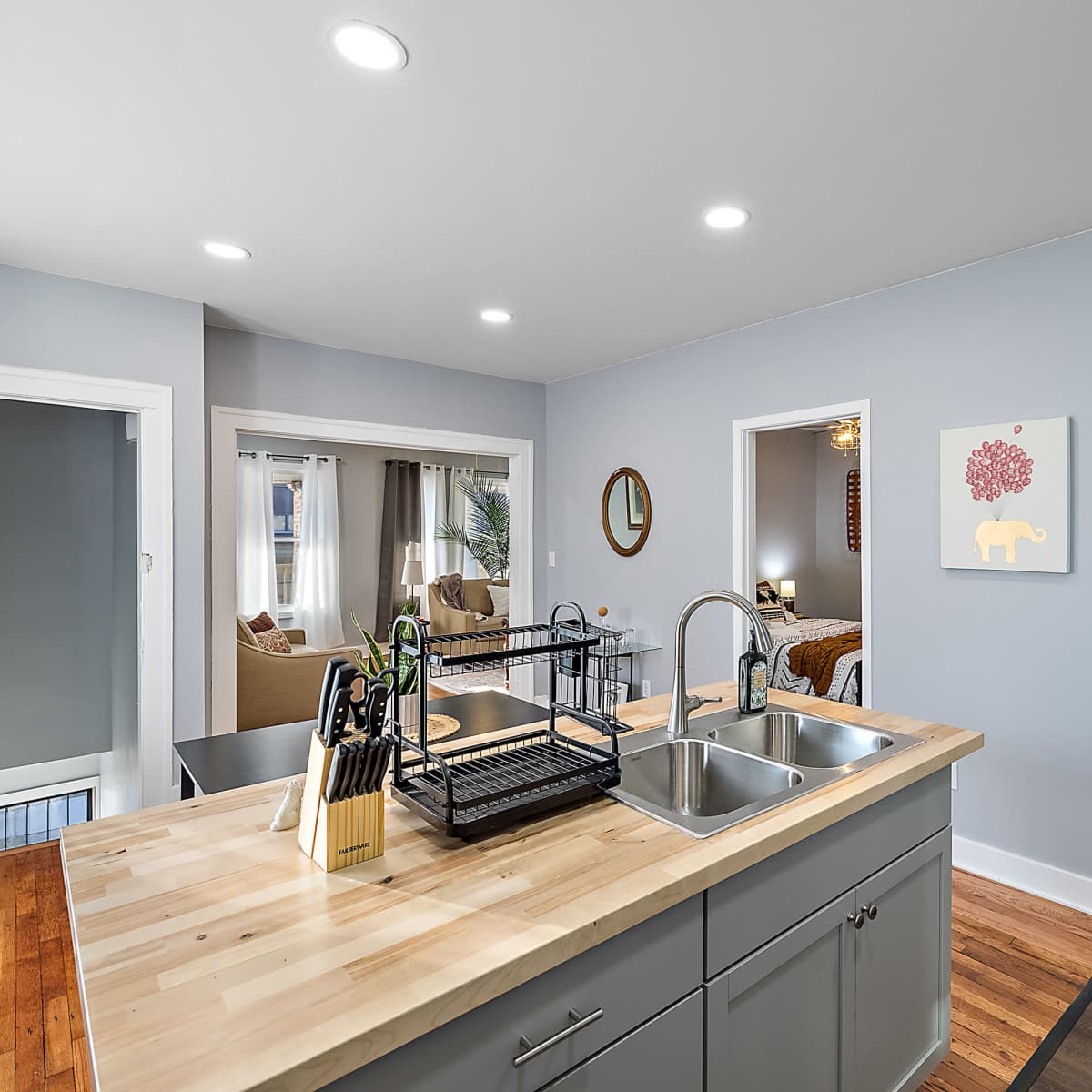 A modern kitchen area with a wooden island featuring a sink, leading to two doorways that open into a living room and a bedroom.