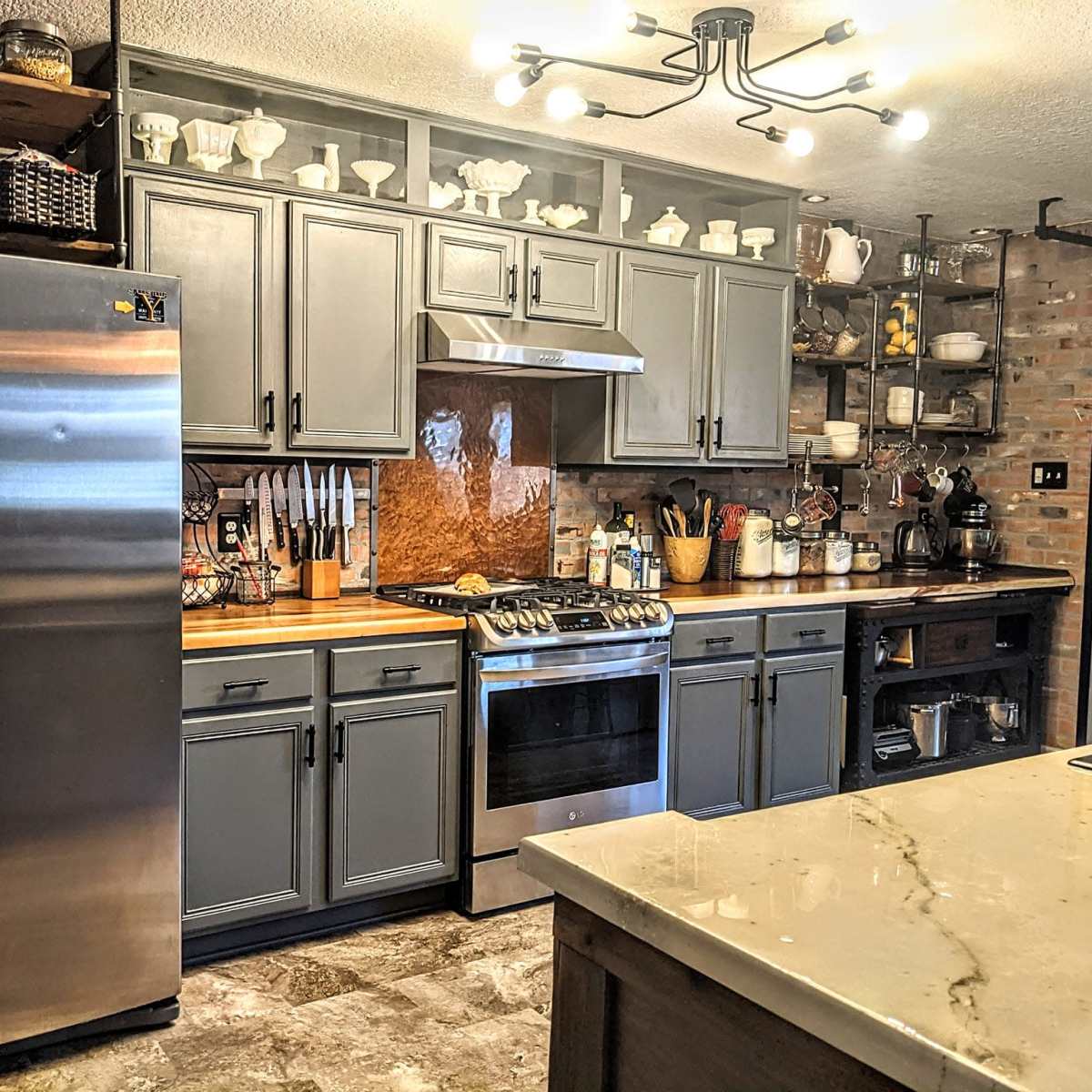 A modern kitchen featuring stainless steel appliances, gray cabinets, and a central island with a marble countertop.