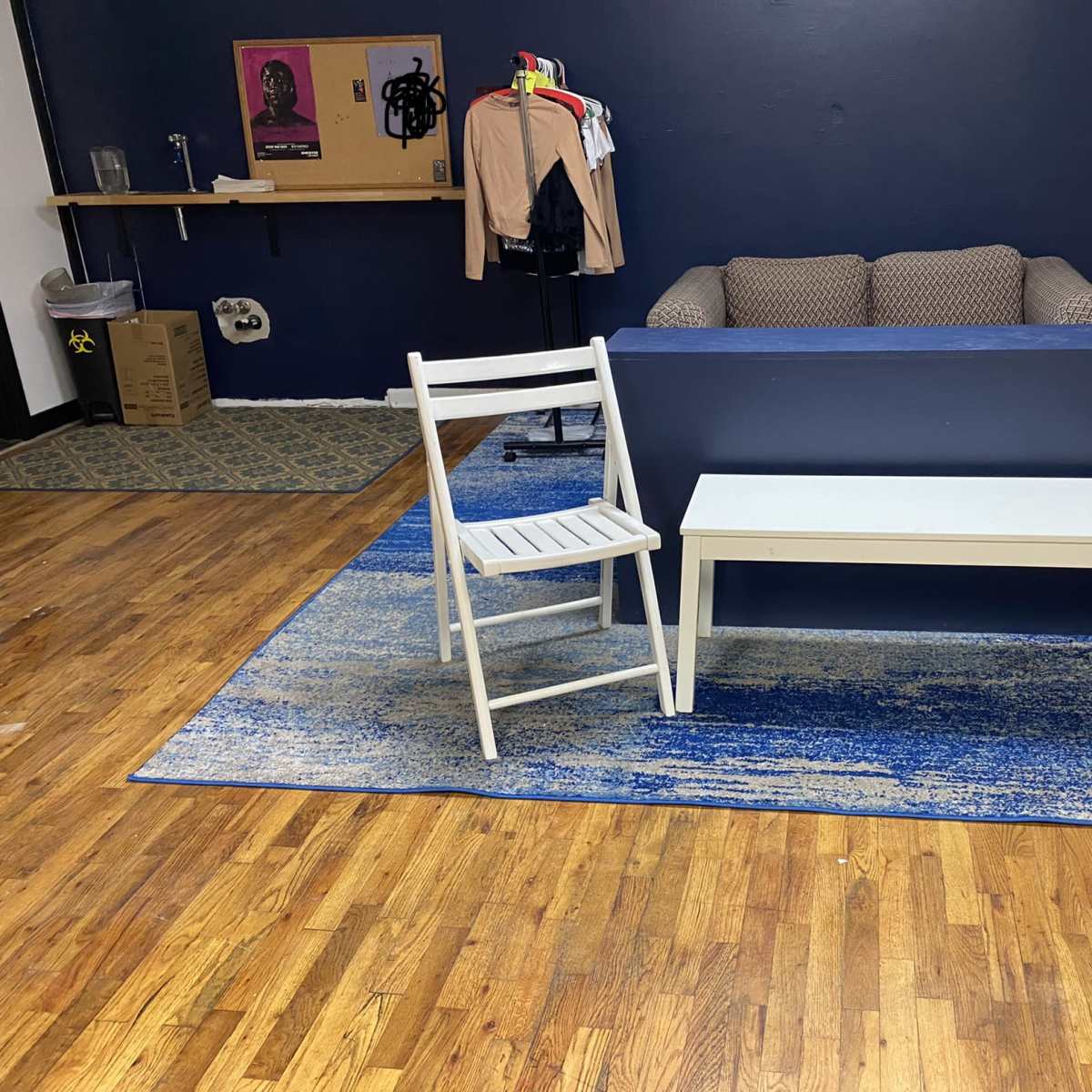 A room with a brown couch against a blue wall, two white chairs, and a light-colored table on a blue rug.