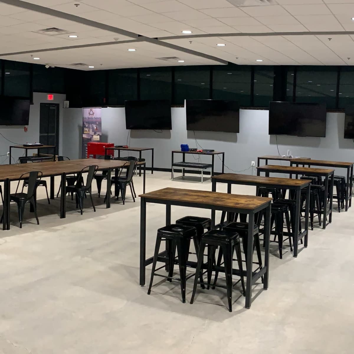 A spacious room with multiple long tables and high-backed stools, equipped with large screens mounted on the walls.