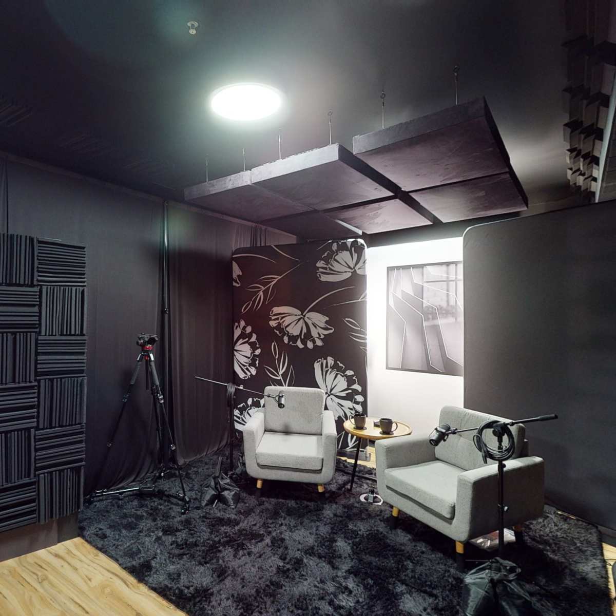 A soundproof studio with two gray armchairs, a small table, and audio equipment set up against a dark wall with sound-absorbing panels.