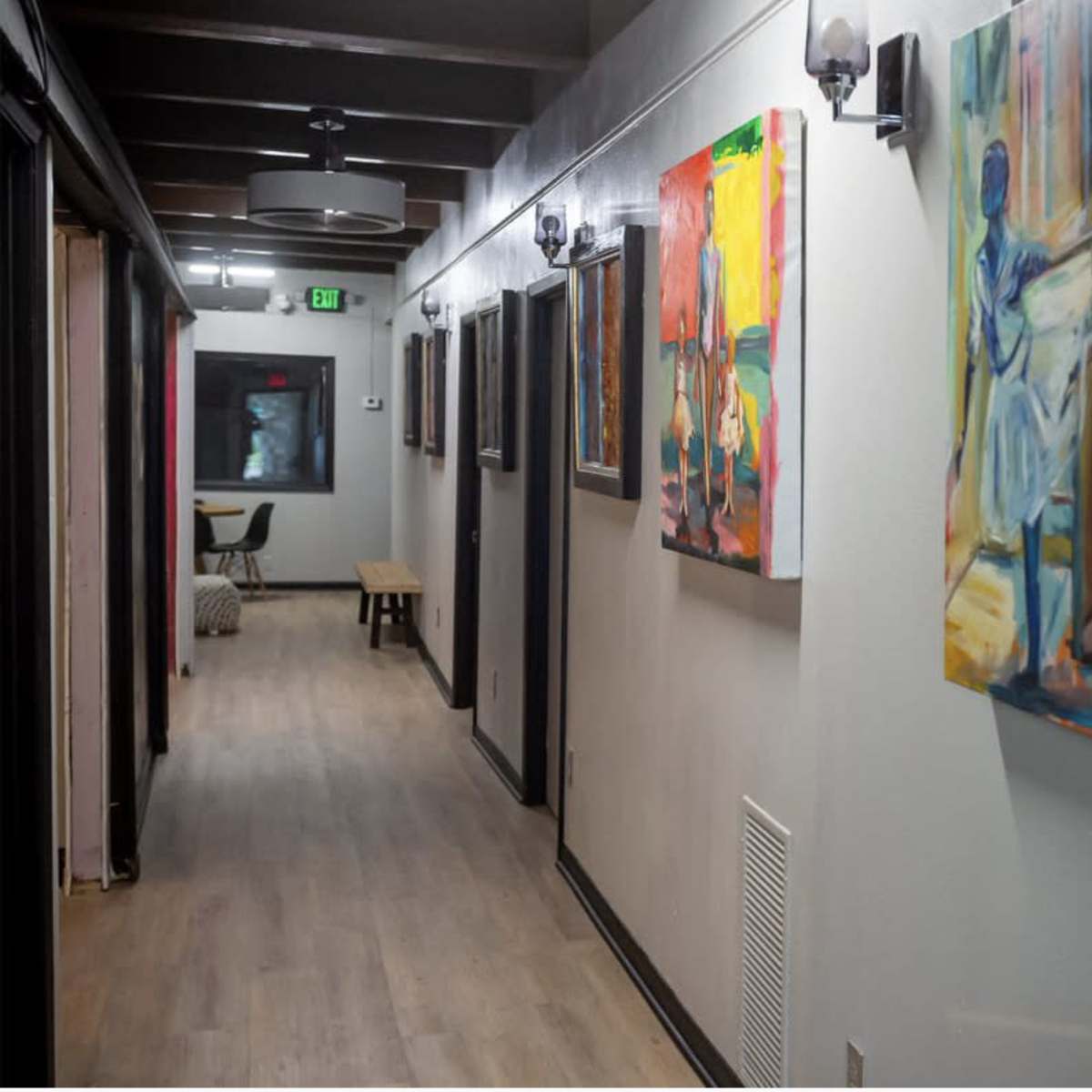 A long, well-lit hallway adorned with abstract paintings on the walls, leading to a small seating area at the far end.