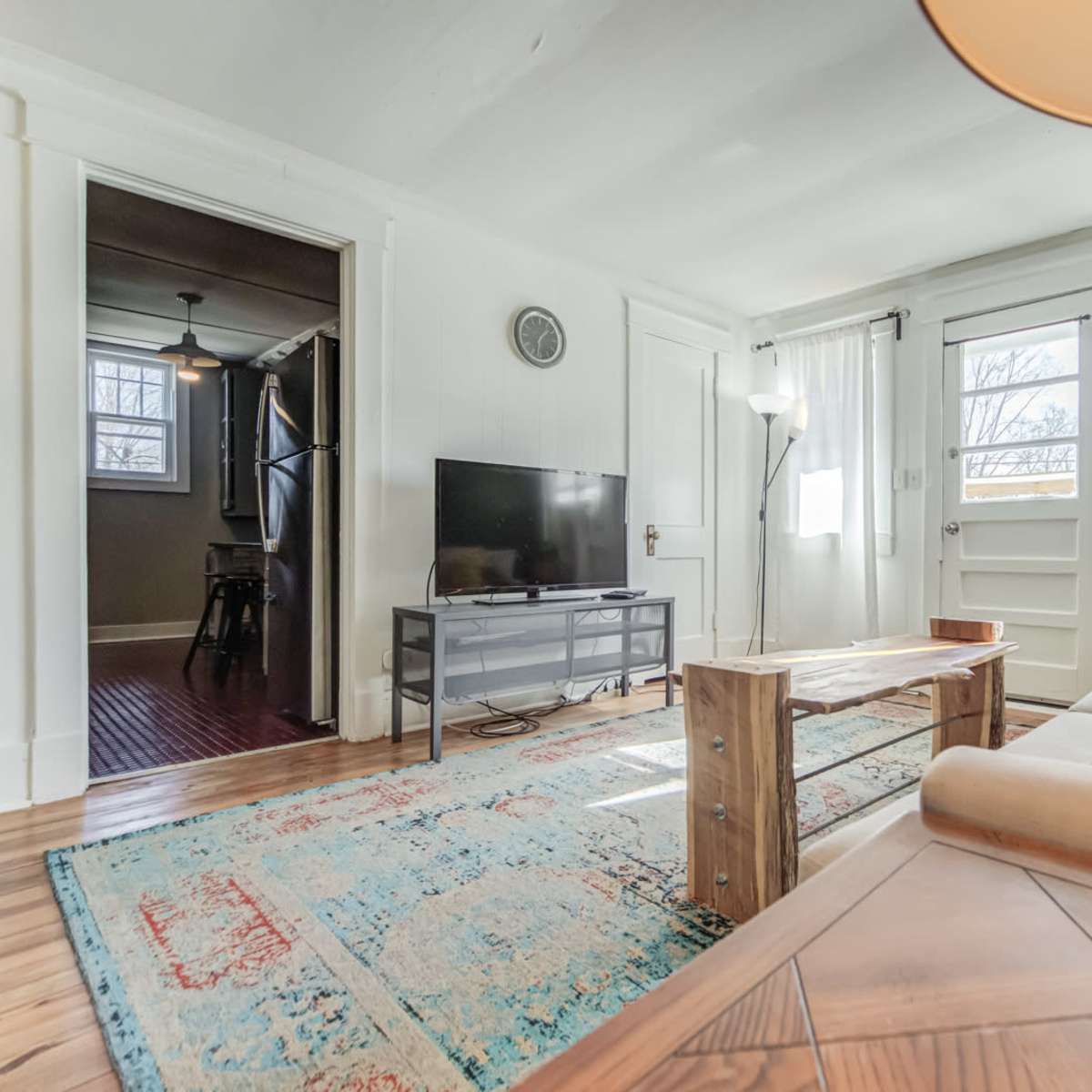 The living room features a couch, a wooden coffee table, a television on a stand, and large windows allowing natural light to enter.