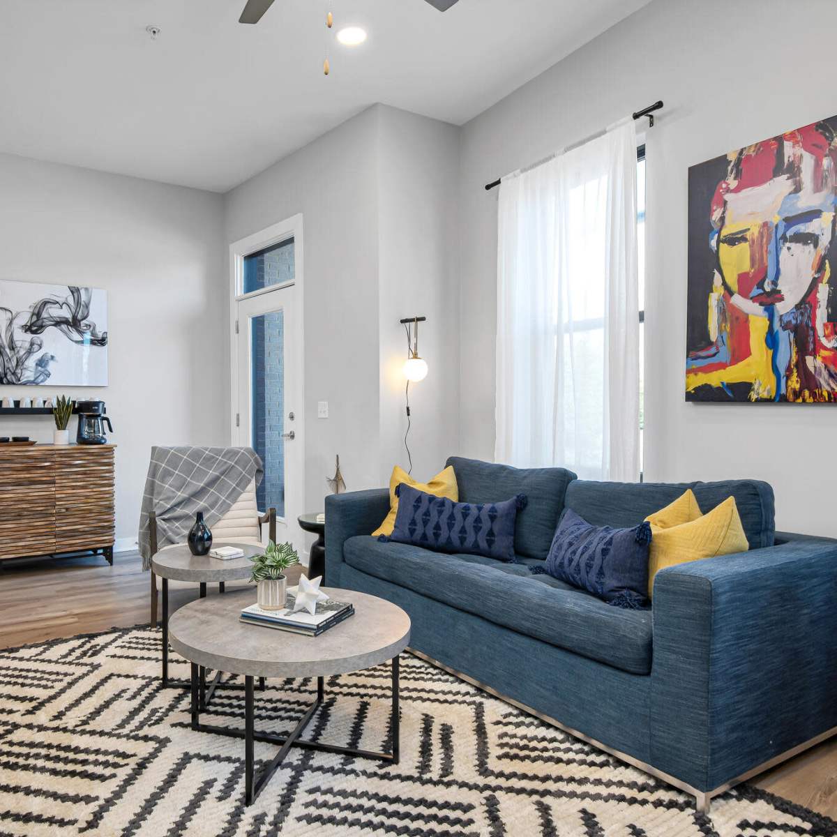 The living room features a blue sofa, a round coffee table, and an abstract painting on the wall, with a modern design and hardwood floors.