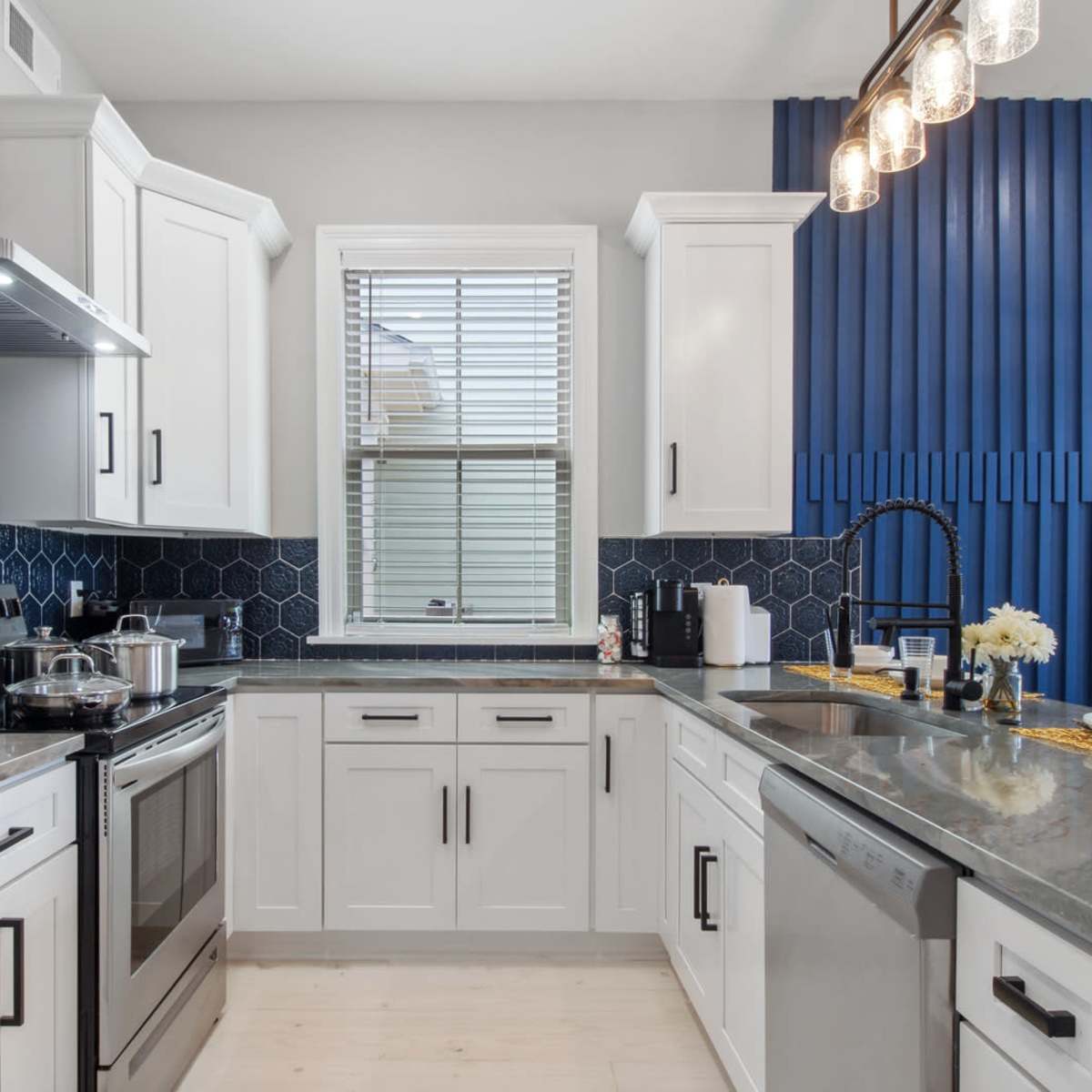 A compact kitchen features white cabinetry, stainless steel appliances, and a blue textured wall accent.