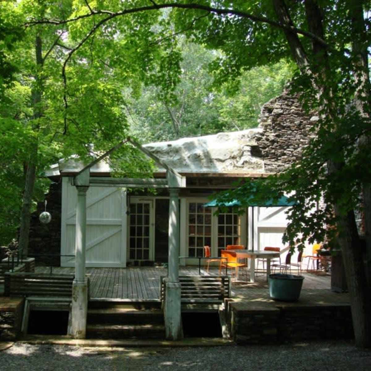 A modern cabin is situated in a wooded area, featuring large glass doors that open onto a wooden deck surrounded by trees.