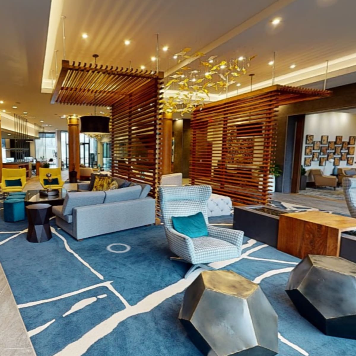 A modern lobby with seating areas, wooden dividers, and a large area rug featuring abstract patterns.