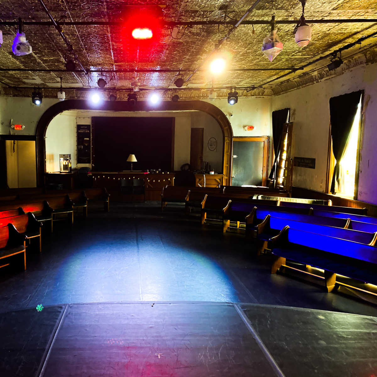 An empty theater space with circular seating arranged around a central stage, illuminated by multicolored lights.