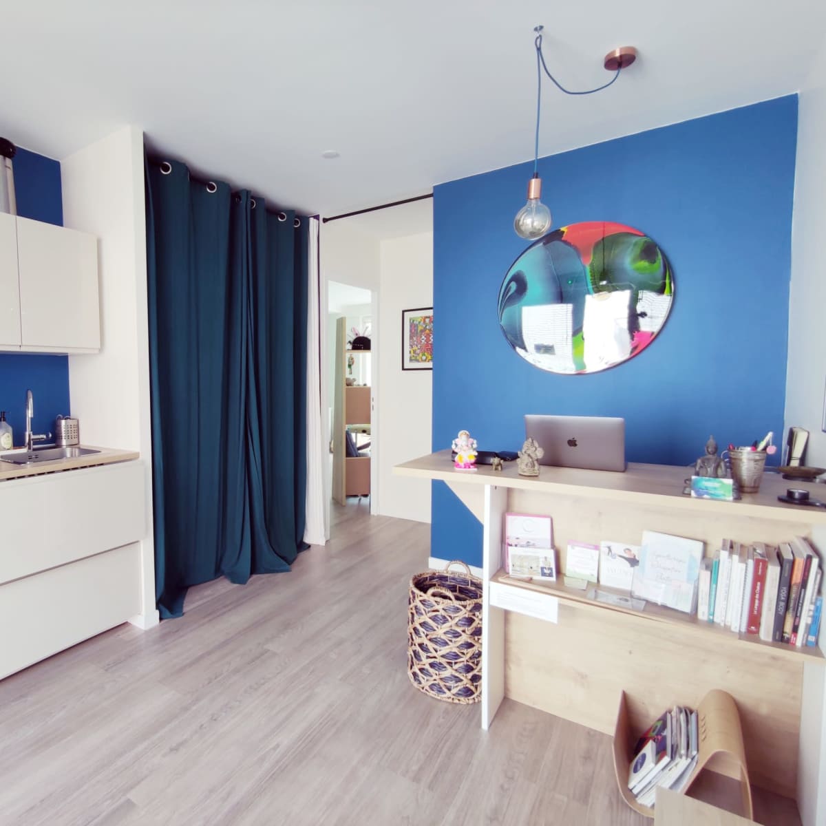 A modern kitchen with beige cabinetry and a blue accent wall, featuring a dining area with a small desk and shelves.