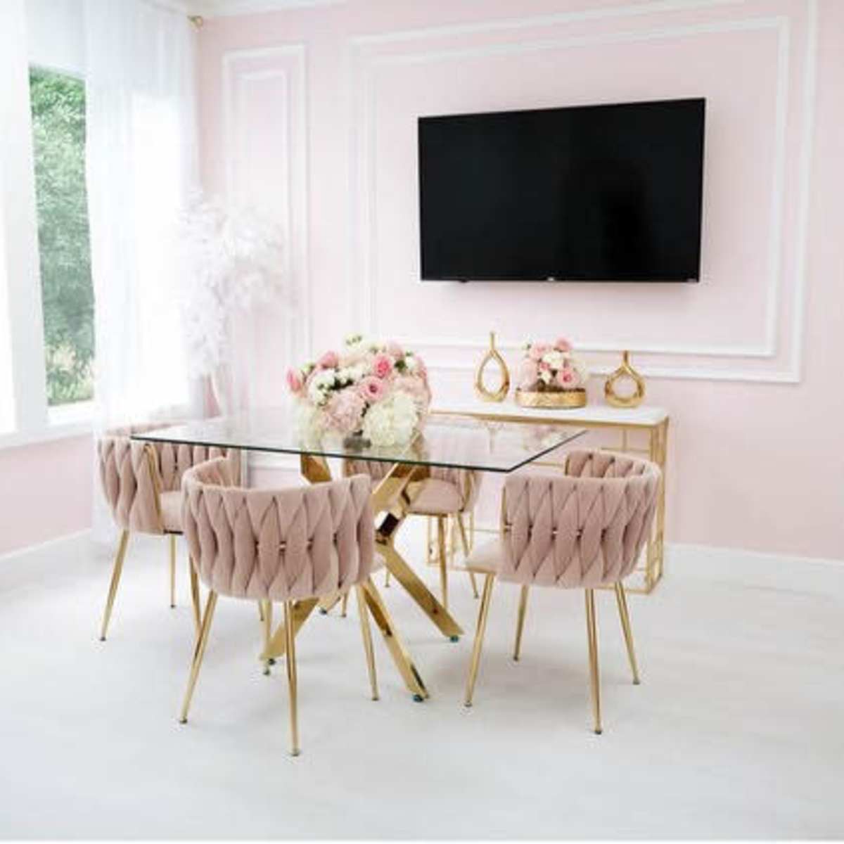 A modern dining area with a glass table surrounded by pink upholstered chairs and a large wall-mounted TV in a softly lit room with pink walls.