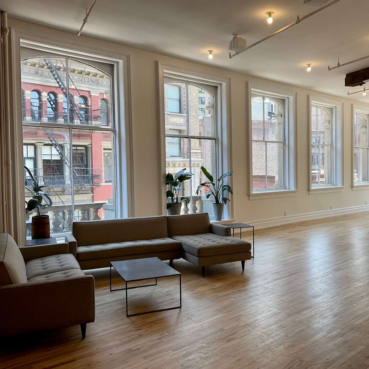 A spacious, well-lit room with large windows, wooden floors, and modern furniture, including sofas and a dining table.