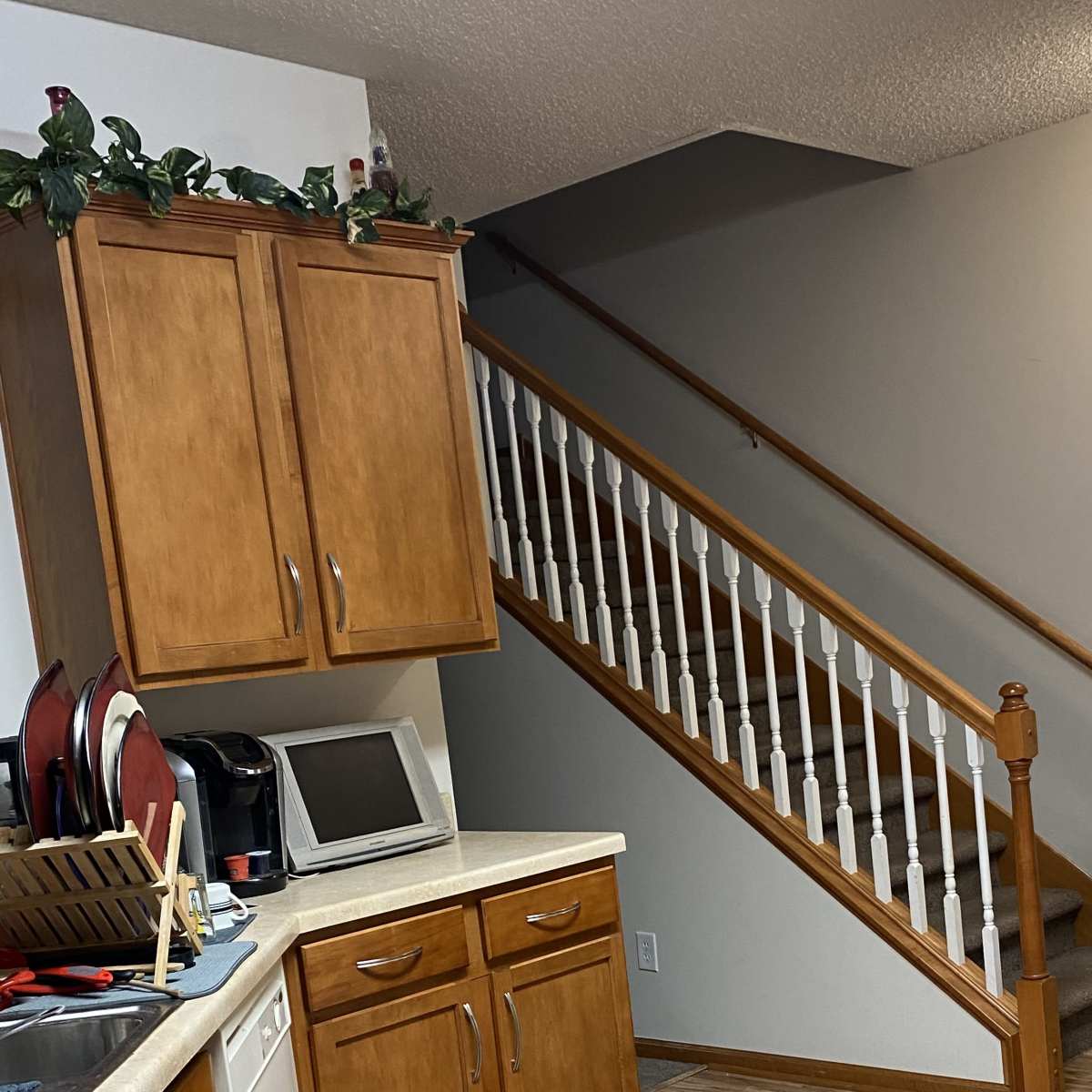 A kitchen area with wooden cabinets, a countertop, and a staircase leading to an upper floor.