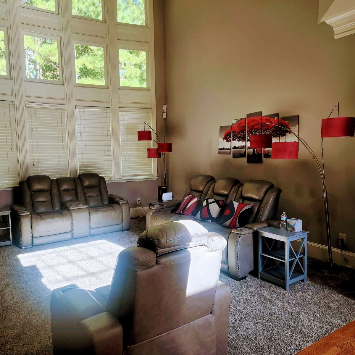 The living room features large windows that allow natural light to illuminate a seating area with gray recliners and side tables.