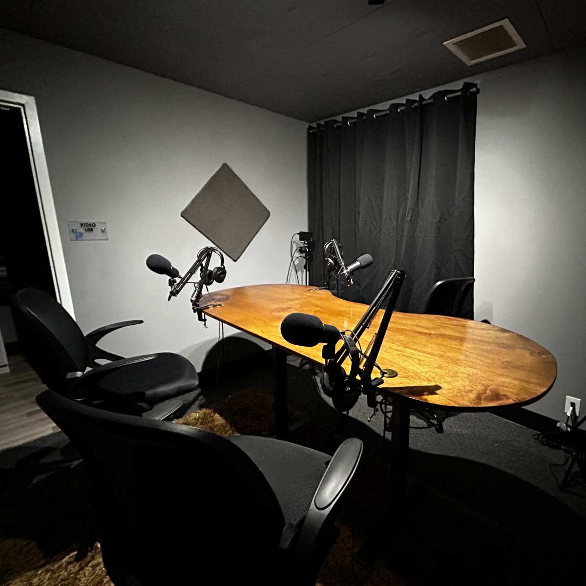 A small recording studio with a large oval table, two chairs, and multiple microphones set up around the table.