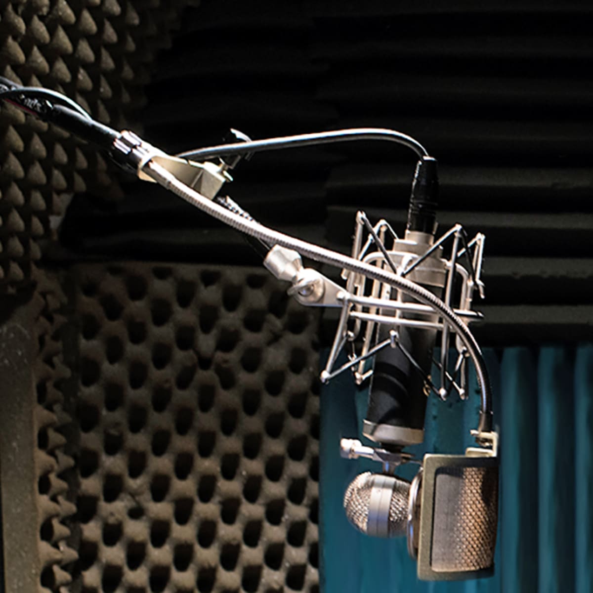 A microphone hangs from a stand in a soundproof recording studio.