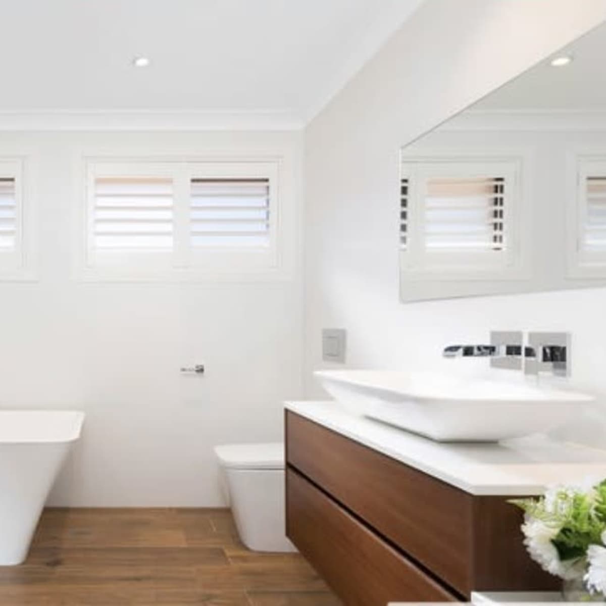A modern bathroom featuring a freestanding bathtub, a wall-mounted sink, and a wooden vanity with a mirror.
