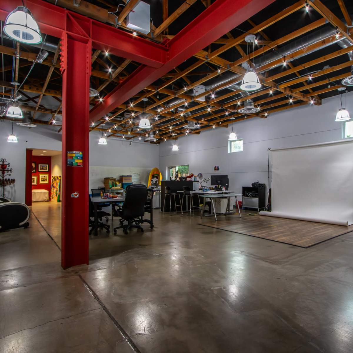 A modern office space with an open layout, featuring several workstations, a backdrop for photography, and various lighting fixtures.