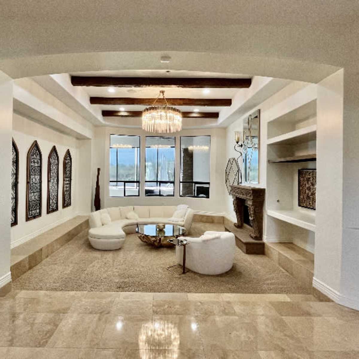 A spacious living room with a circular seating arrangement, a chandelier, large windows, and a stone fireplace.