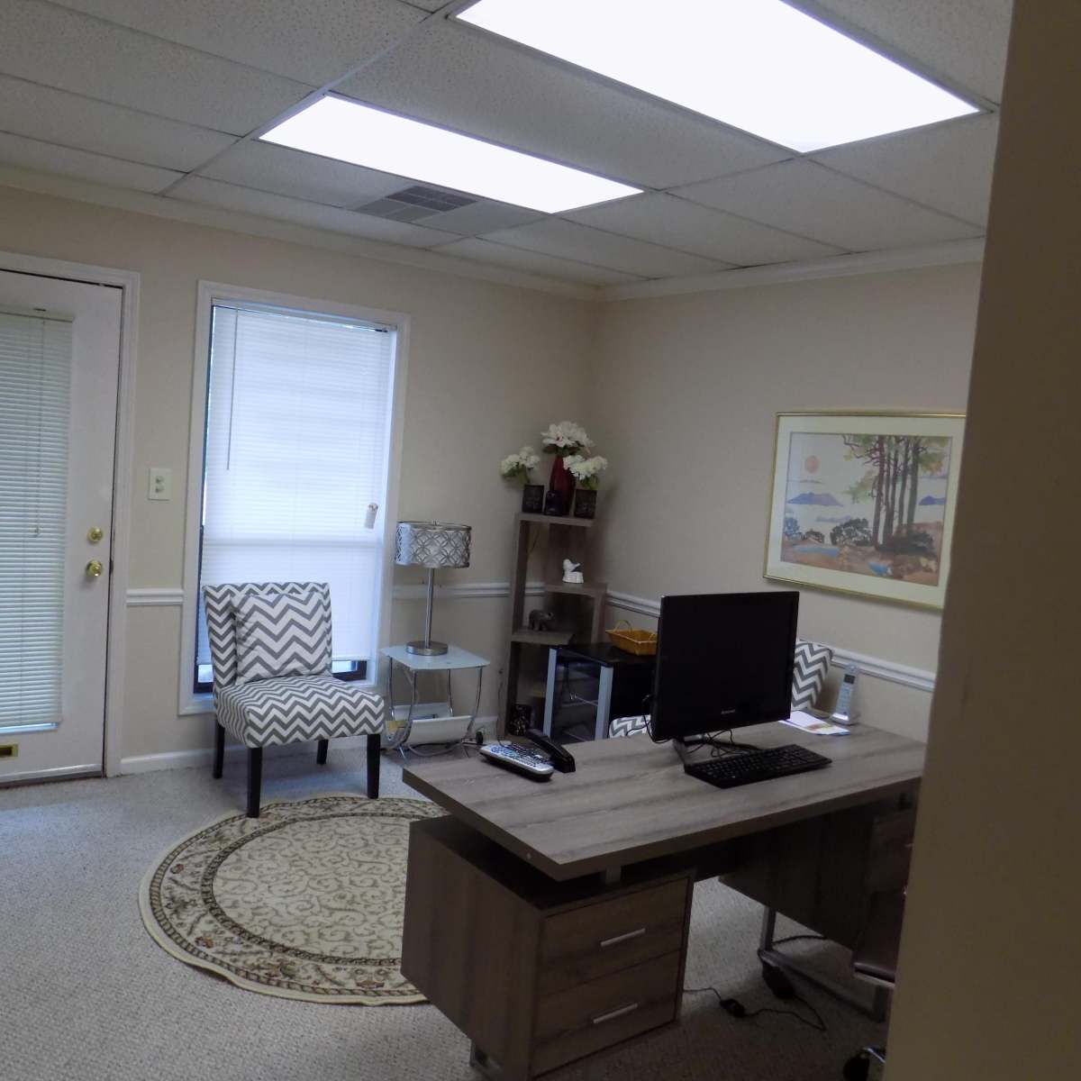 A small office space with a desk, computer, two chairs, and a decorative rug.
