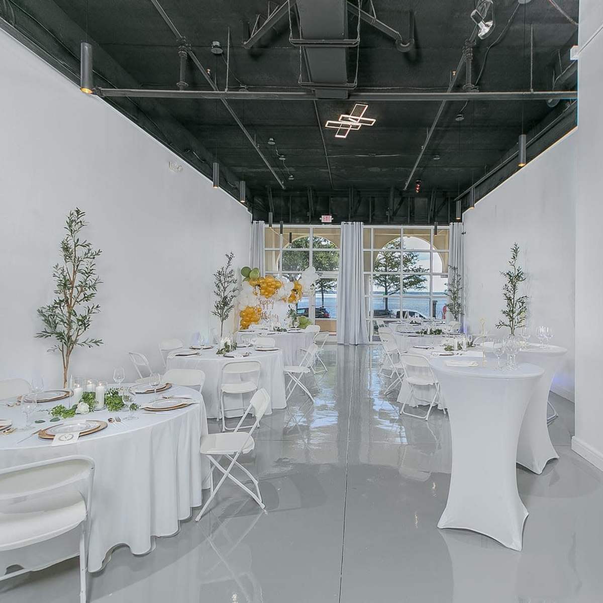 A spacious, modern event venue with white walls, polished floors, and tables set for a gathering.