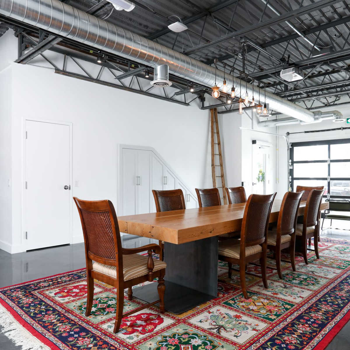 A modern meeting space with a wooden table, ten chairs, a brick wall, and a decorative rug on a polished floor.