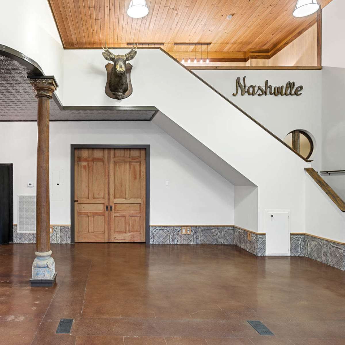 A well-lit entryway featuring wooden columns, a mounted moose head, and a staircase leading to an upper level.