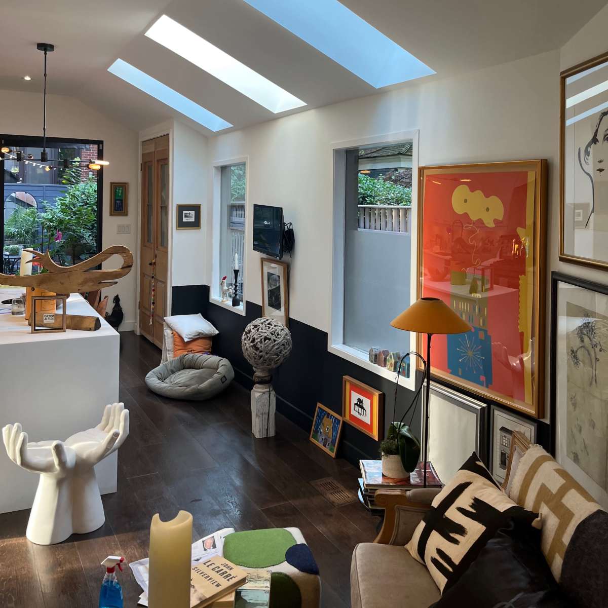 A modern interior space featuring skylights, various artworks on the walls, and a mix of decorative furniture.