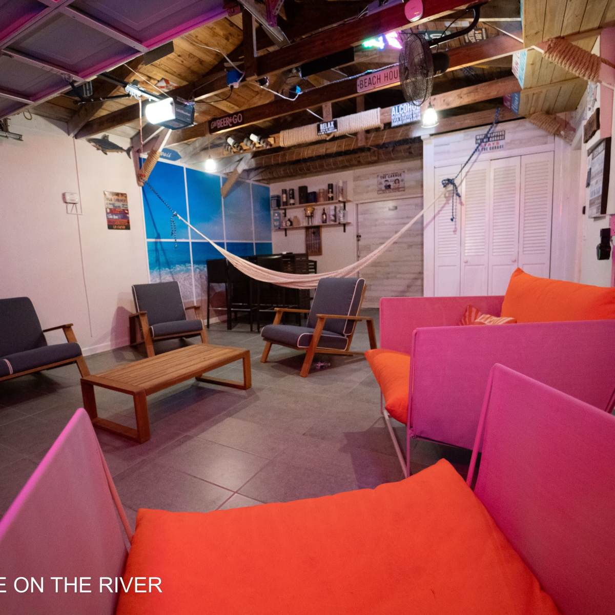 A casual lounge area with gray and pink seating, a wooden coffee table, and a hammock, set against a backdrop of beach-themed decor.