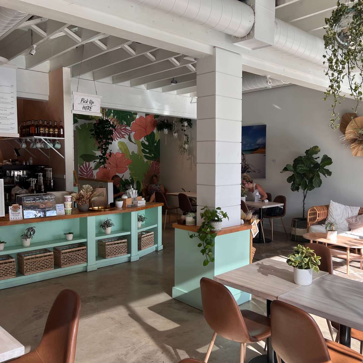A bright café interior with green accents, plants, and a mix of seating options, including chairs and a cozy lounge area.