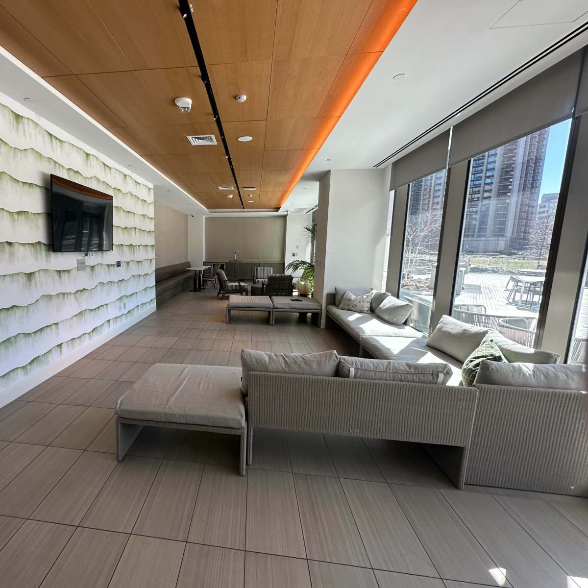 A modern lounge area features a textured green accent wall, multiple seating arrangements, and large windows allowing natural light.