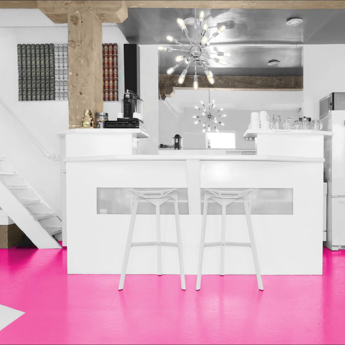 A modern kitchen with a white bar counter and stools, pink flooring, and a staircase in the background.