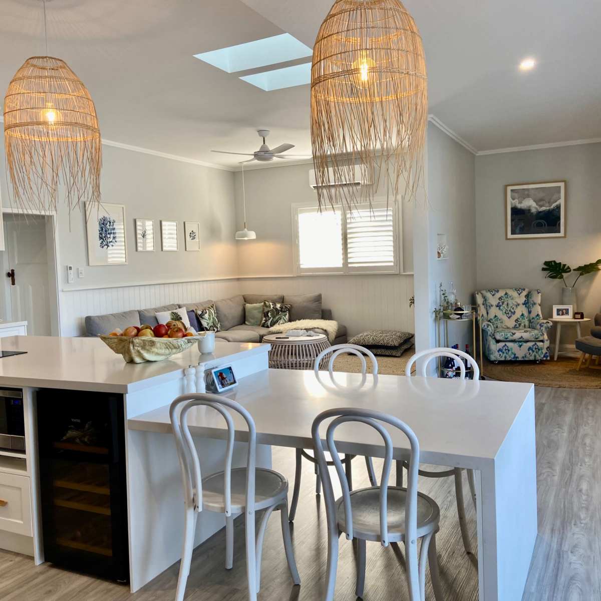 A bright, open-concept living space featuring a kitchen island with chairs, a comfortable seating area with decorative pillows, and natural light streaming in through a skylight.