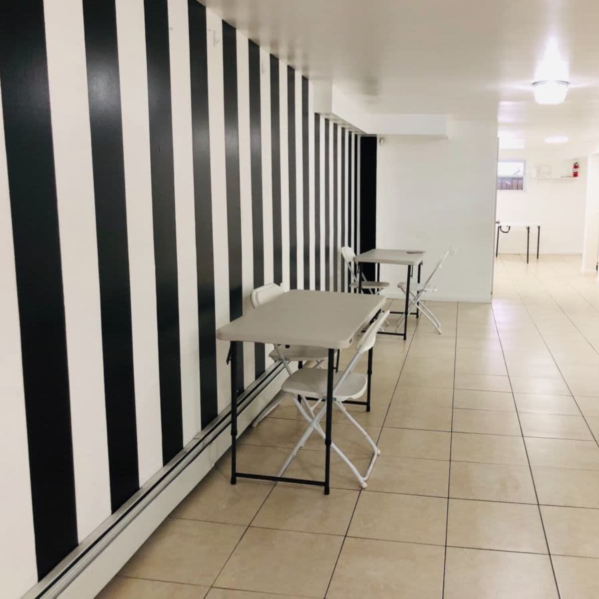 A wide corridor with a striped wall, two folding tables, and tiled flooring in a well-lit area.
