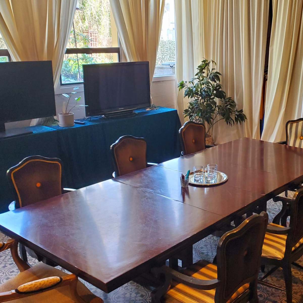 A spacious dining area features a large wooden table surrounded by chairs, with a television and a potted plant in the background.